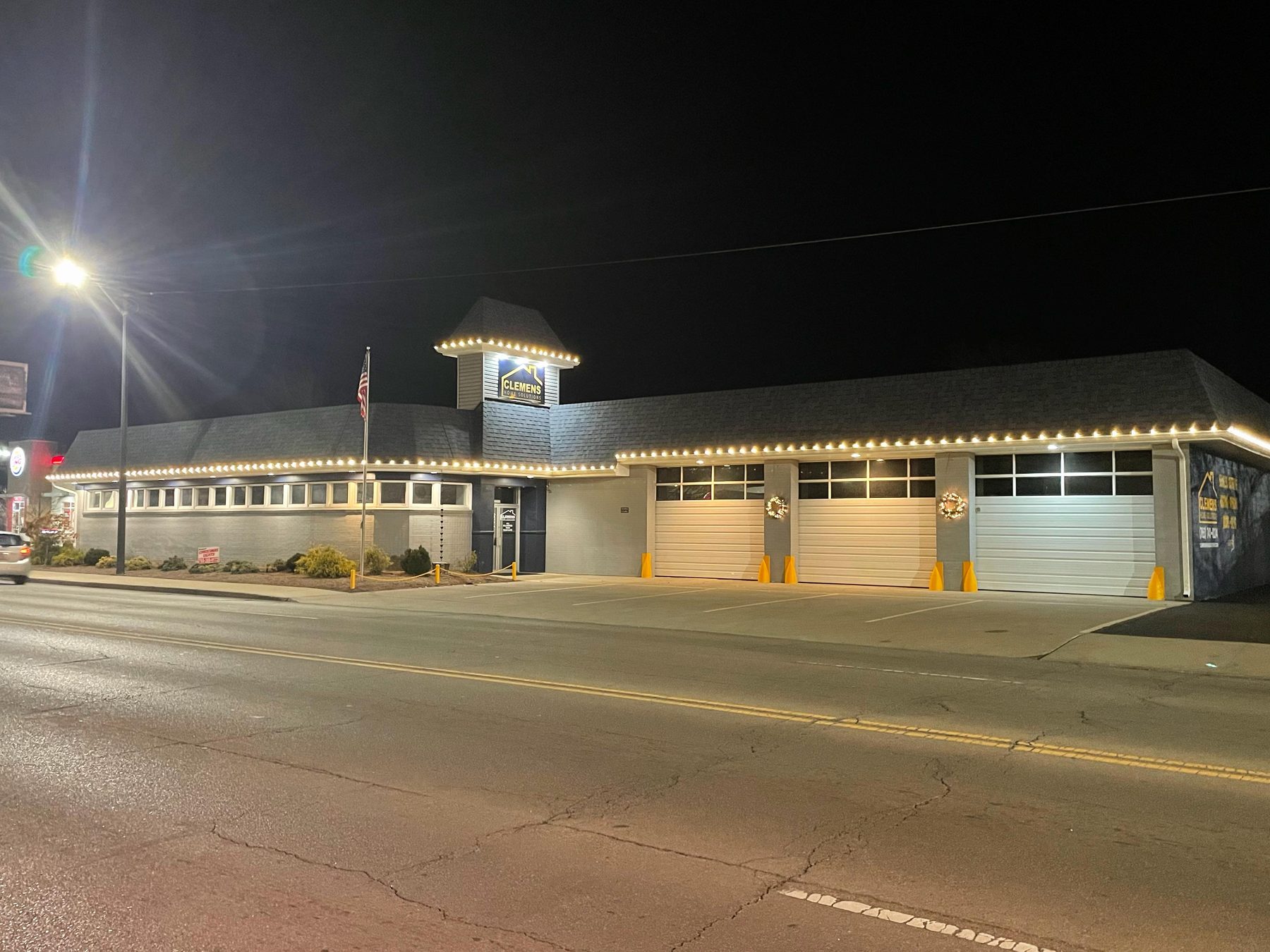 Long Indiana commercial building with warm white C9 Christmas lights along the full roofline and the cupola, and lighted wreaths across the front