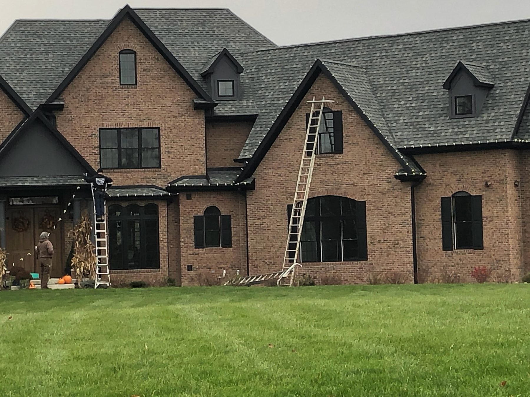 Indiana Christmas Light Installers crew fitting warm white lights along the roofline of a large brick home during a daytime install