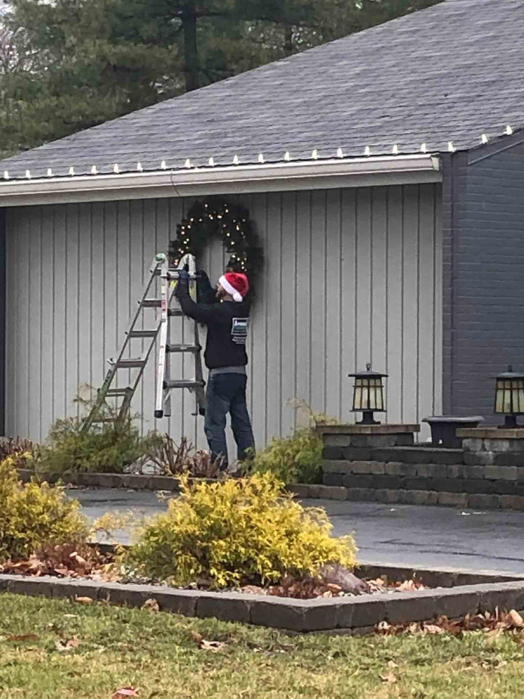 Crew member on a ladder hanging a large lighted Christmas wreath on the front of a home