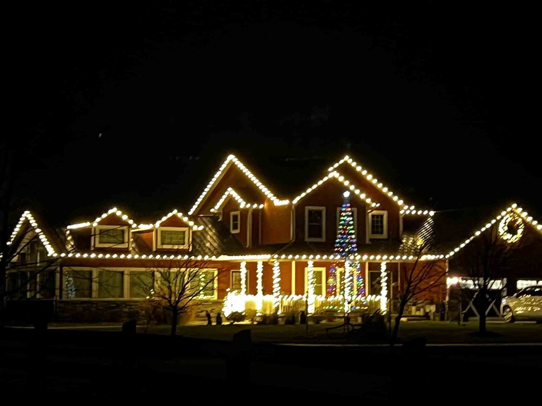 Large Indiana home lit in warm white Christmas lights with a decorated tree beside the porch