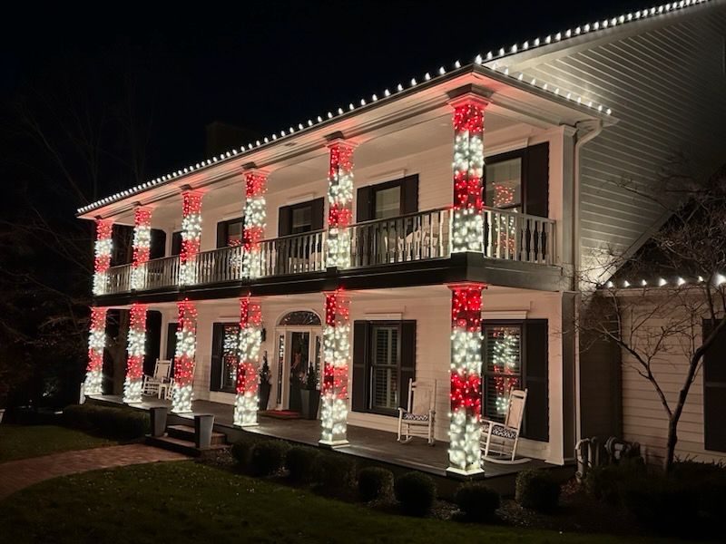 Two story Indiana home with warm white Christmas lights along the roofline and every porch column wrapped in red and white lights