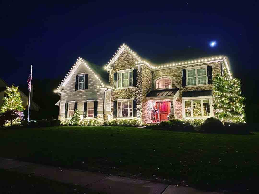 Indiana home lit with warm white Christmas lights beside a fully lit outdoor Christmas tree