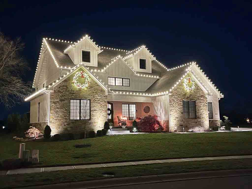 Two story Indiana home with warm white Christmas lights following four separate roof peaks