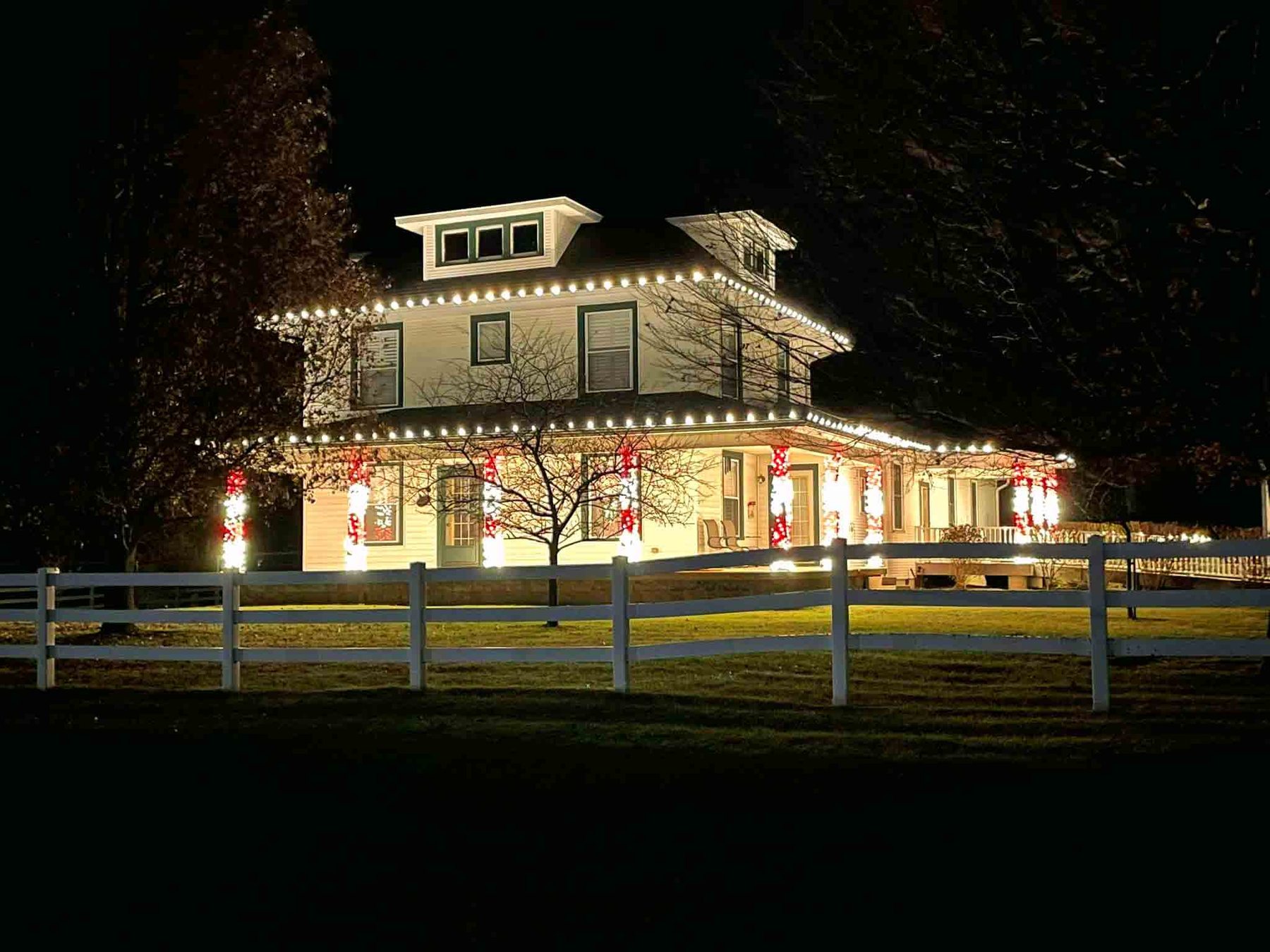Indiana home with a wraparound porch lit in warm white Christmas lights and red decorations