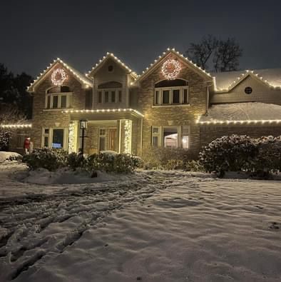 Stone Indiana home lit with warm white Christmas lights and lighted wreaths on the gables, with snow across the front lawn