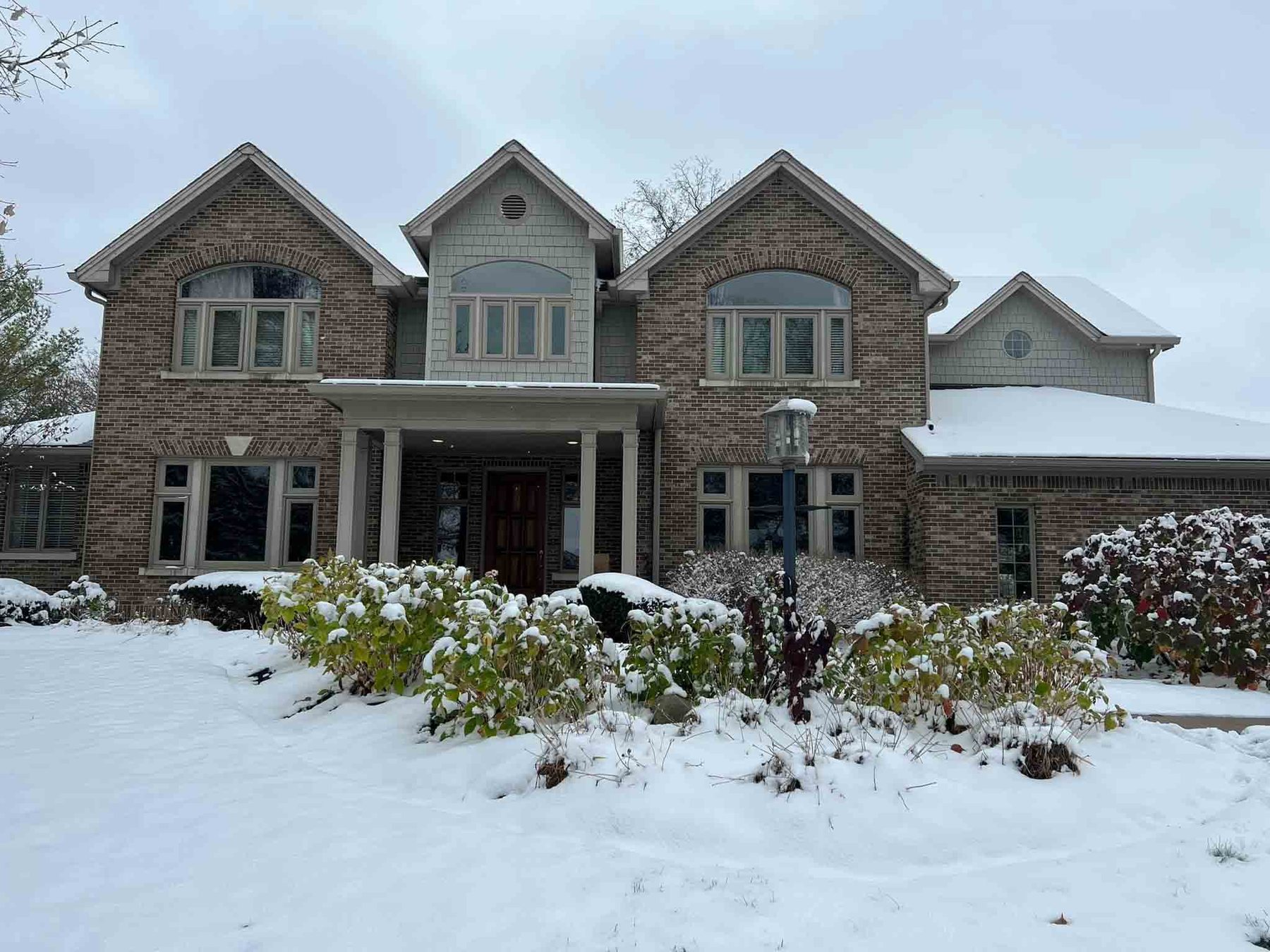 Large brick Indiana home with warm white Christmas lights and snow across the front garden