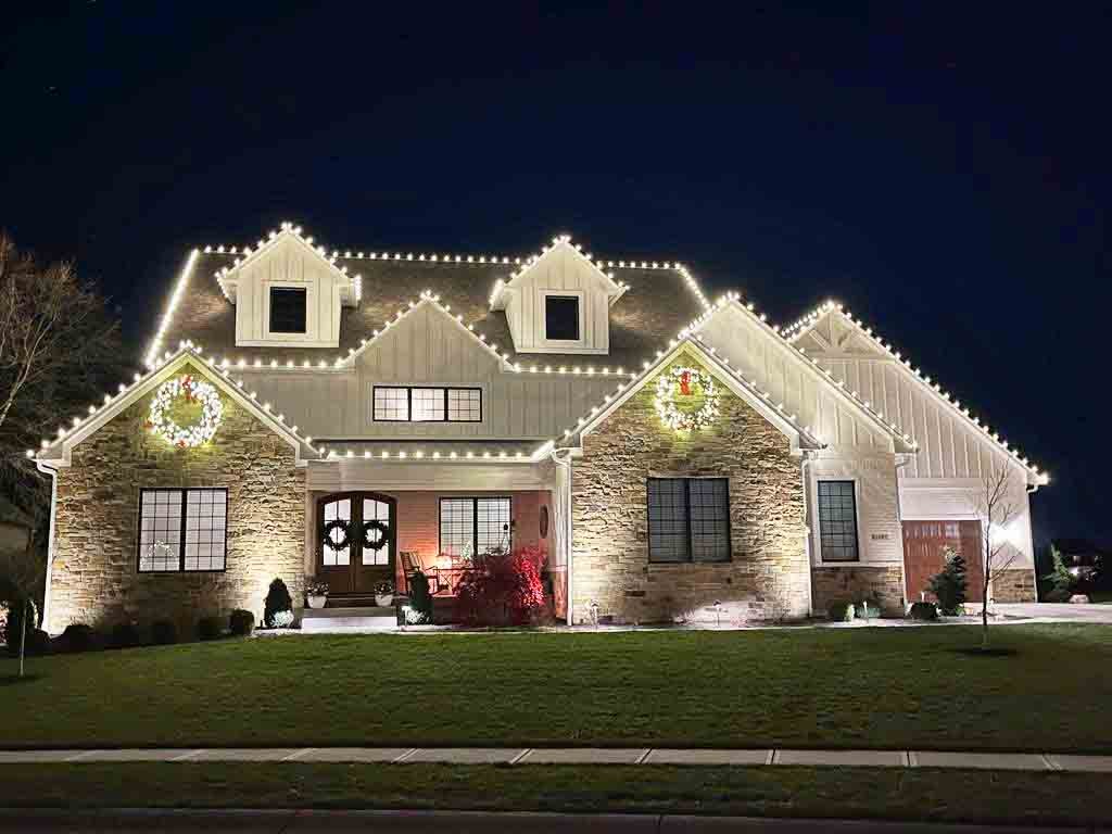 Stone Indiana home with warm white Christmas lights following every gable and roofline, with lighted wreaths on the gables